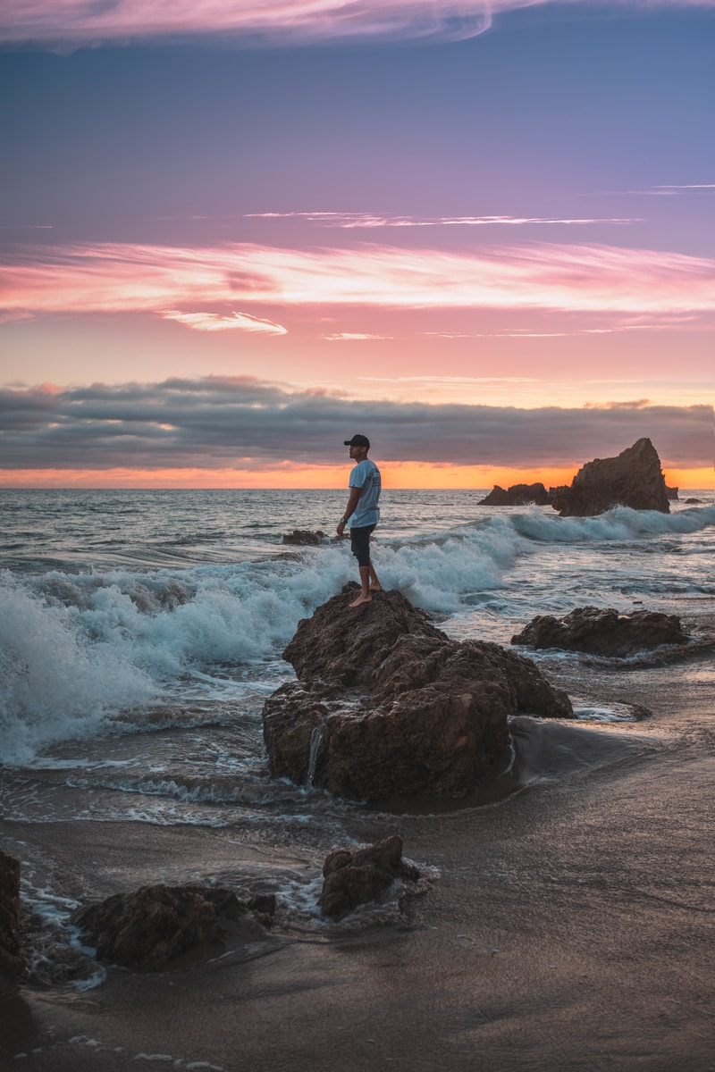 man standing on rock with waves during daytime